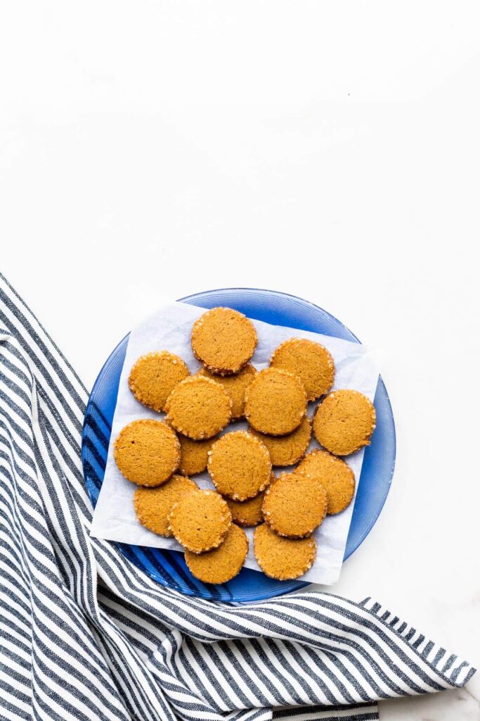 A plate of round gingerbread cookies with crunchy turbinado sugar edges served with a cup of coffee.