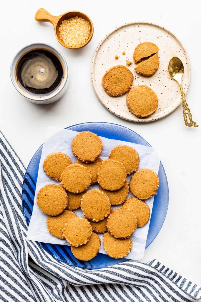 A plate of round gingerbread cookies with crunchy turbinado sugar edges served with a cup of coffee.