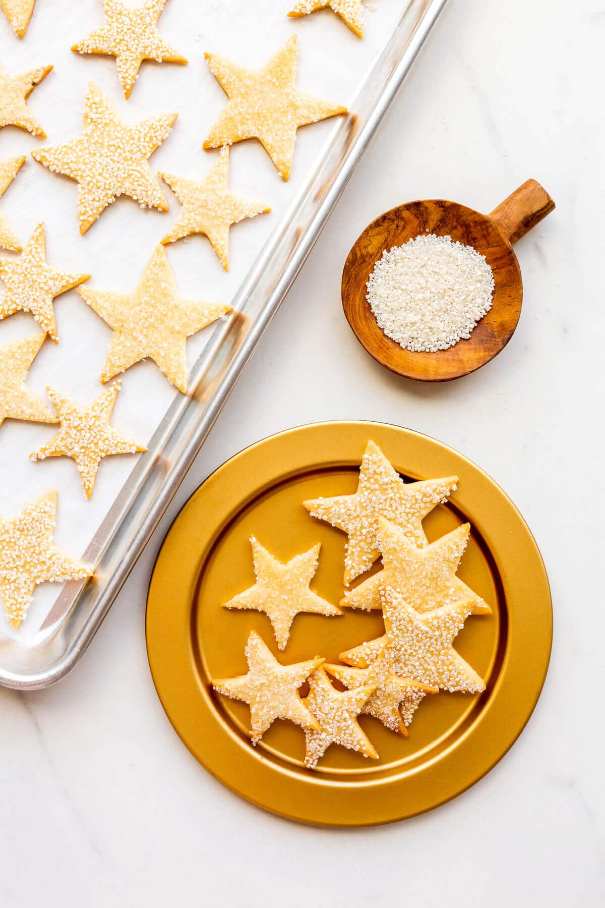 Cut-out sugar cookies shaped like stars and coated in sparkly sanding sugar served on a gold plate.