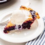 A slice of blueberry pie served à la mode with a scoop of vanilla ice cream on top, melting slowly.