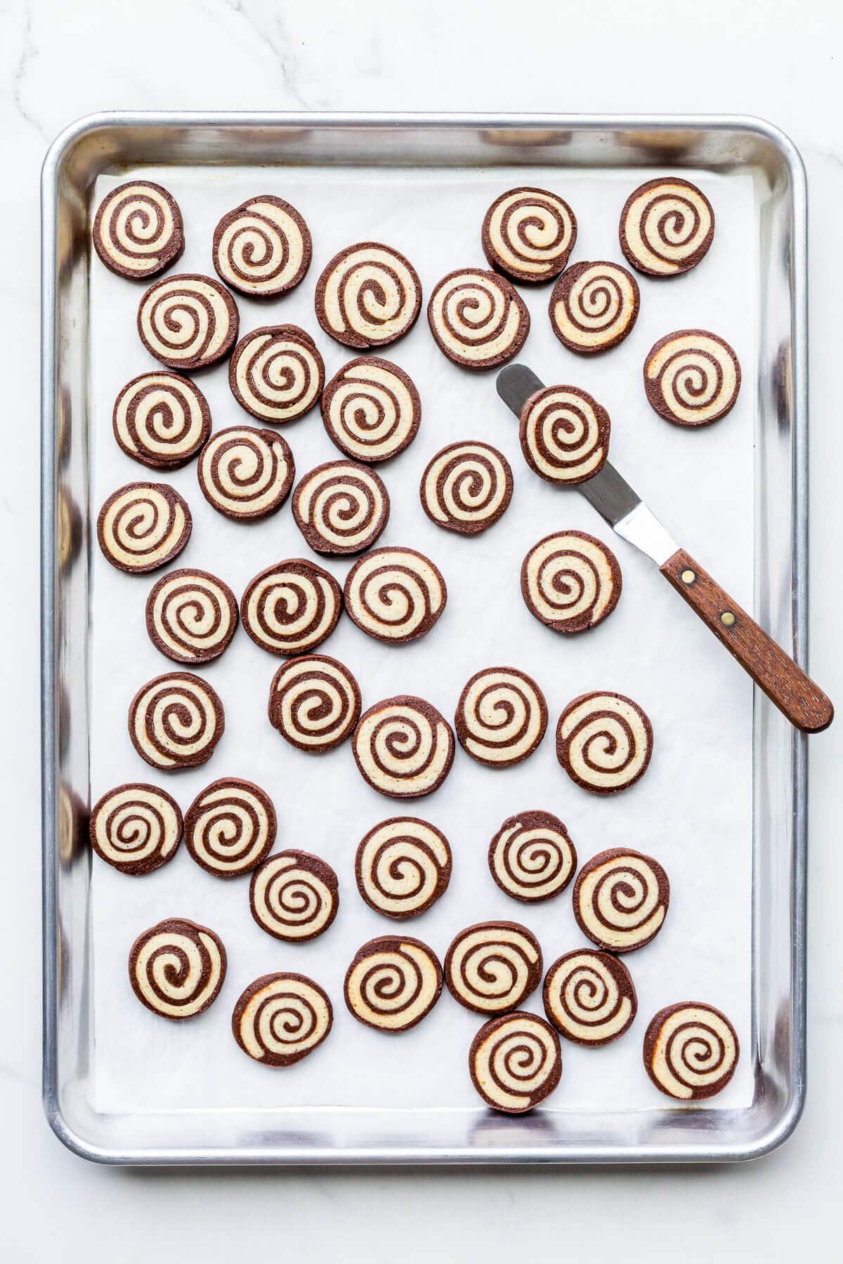 A sheet pan of freshly baked chocolate and vanilla pinwheel cookies.