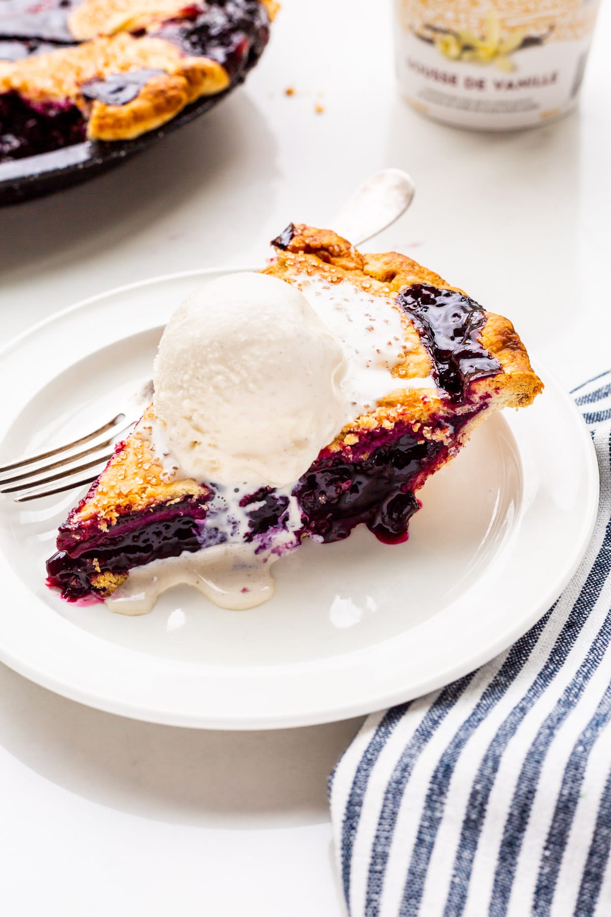 A slice of blueberry pie served à la mode with a scoop of vanilla ice cream on top, melting slowly.