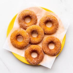 A yellow plate of baked pumpkin donuts coated in cinnamon sugar.
