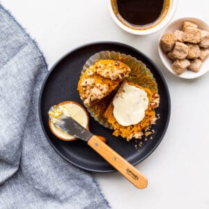 A plate with a pumpkin muffin split open and smeared with butter, with a cup of coffee on the side.