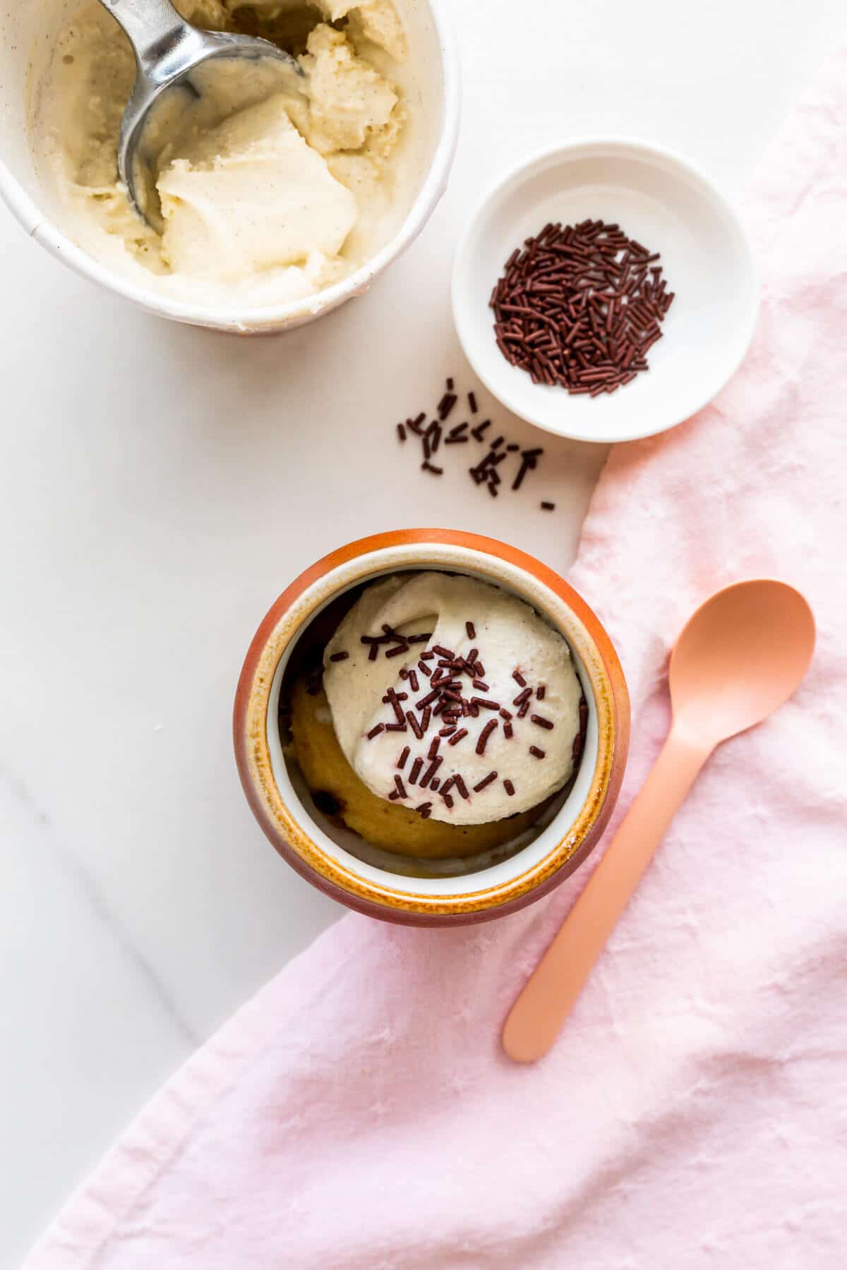 Vanilla mug cake with chocolate chips, topped with ice cream and sprinkles.