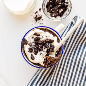 Oreo mug cake topped with whipped cream and crushed Oreo cookies.