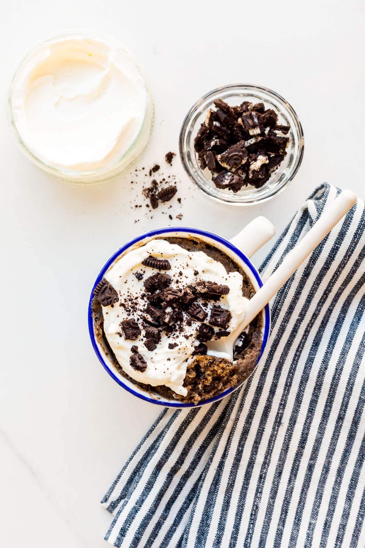 Image of Oreo mug cake topped with whipped cream and crushed Oreo cookies.