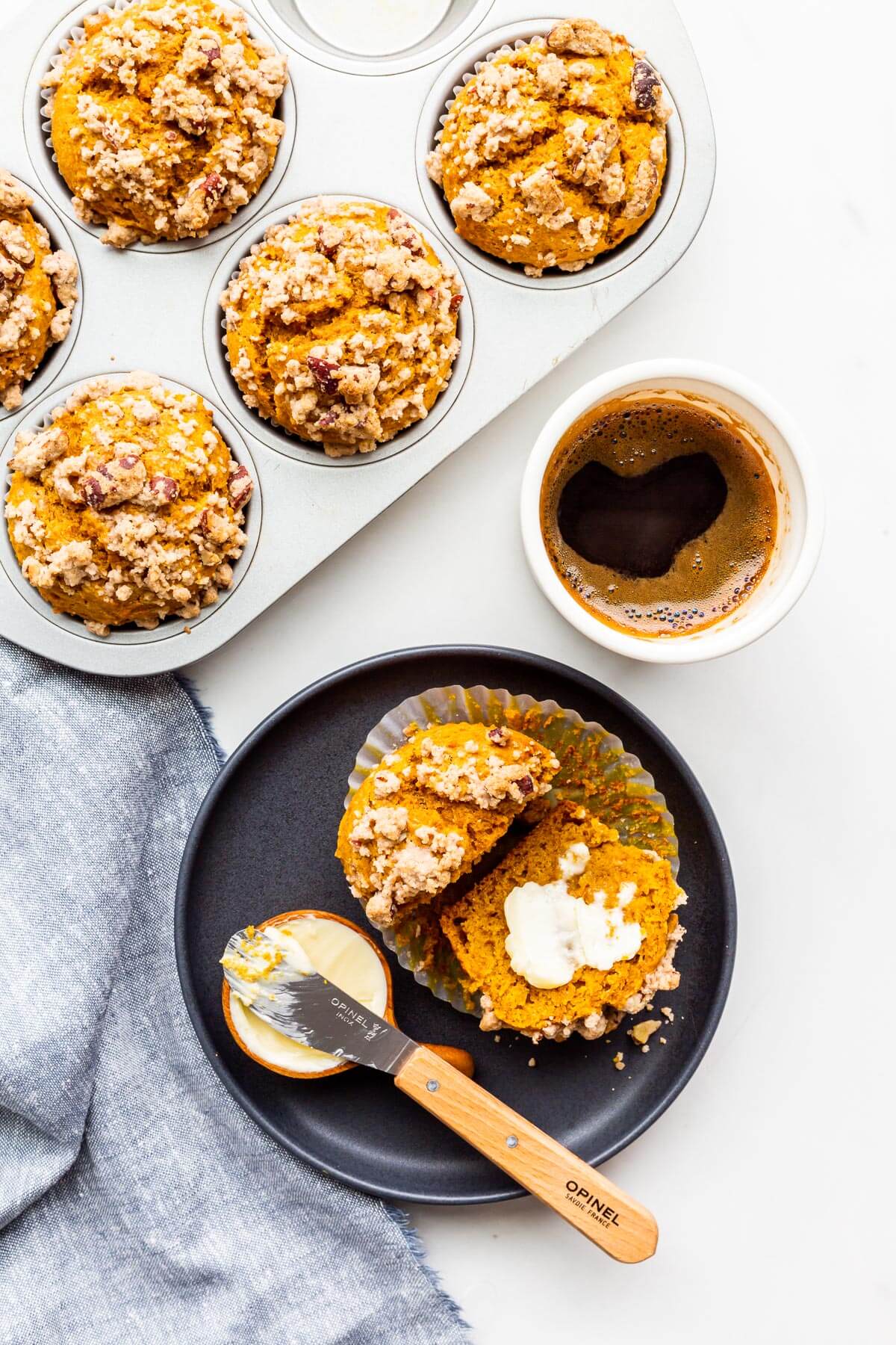 A plate with a pumpkin muffin split open and smeared with butter, with a cup of coffee on the side.