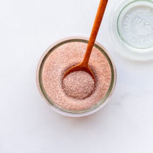 An open jar of cinnamon sugar with a wooden spoon.