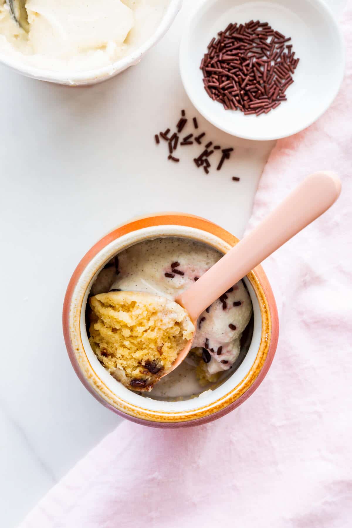 Chocolate chip mug cake cooked directly in a mug and served with ice cream and chocolate sprinkles.