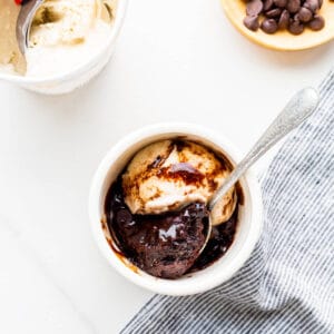 Chocolate mug cake topped with ice cream and chocolate sauce.