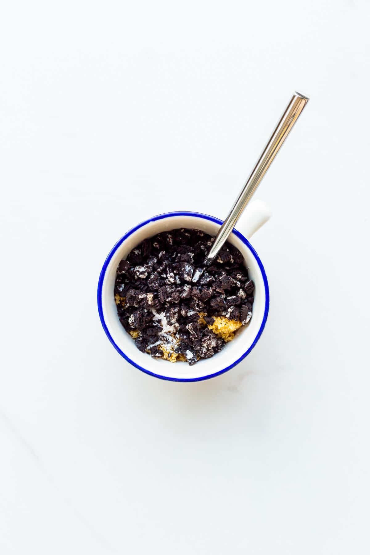 Image of dry ingredients in a mug to make an Oreo mug cake including crushed Oreo cookies and light brown sugar.