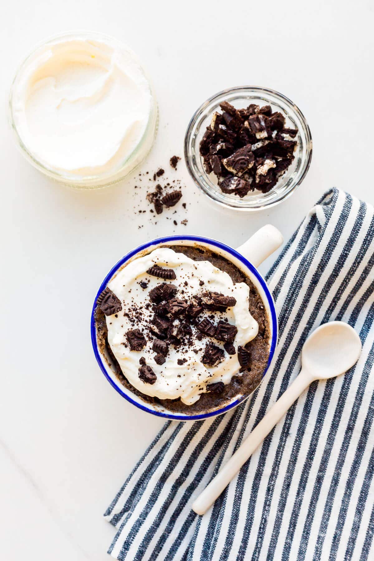 Image of Oreo mug cake topped with whipped cream and crushed Oreo cookies.