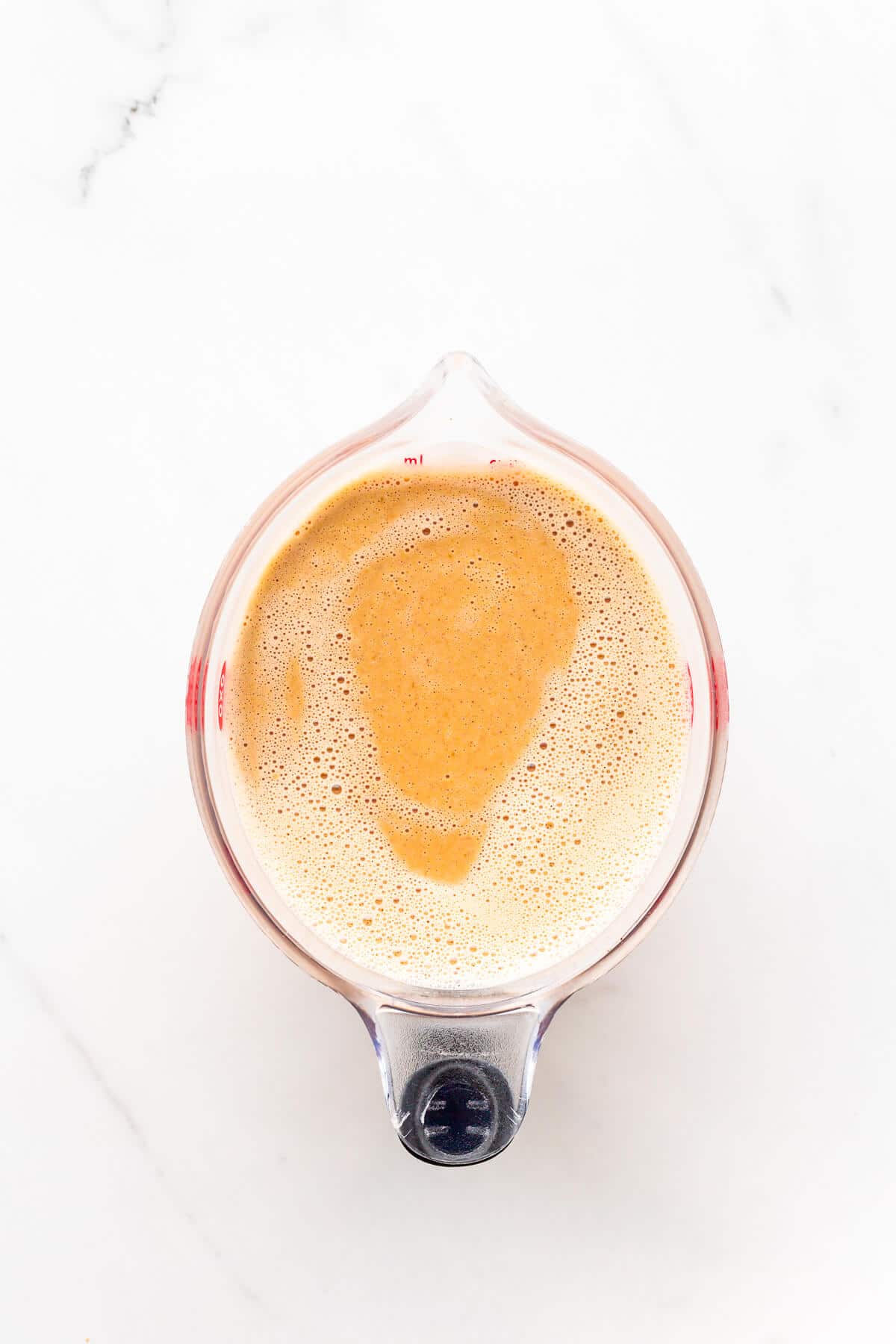 Pumpkin custard in a 1 litre measuring cup with a pouring spout, ready to be churned in an ice cream machine to make homemade pumpkin ice cream.