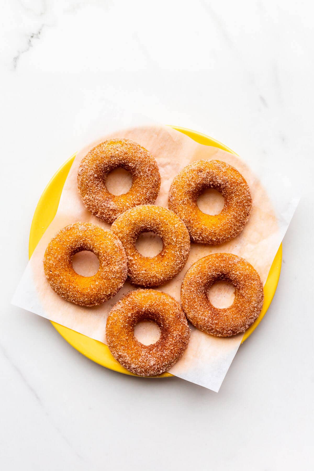 A yellow plate of baked pumpkin donuts coated in cinnamon sugar.