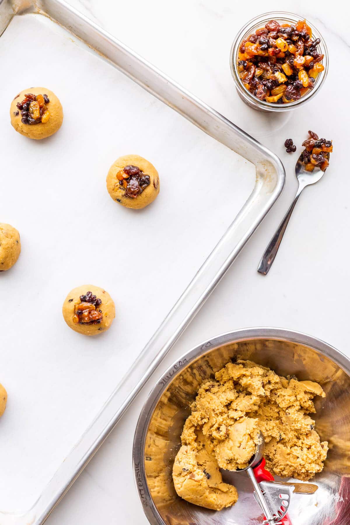 Scooping mincemeat cookie dough and topping with more mincemeat before baking.