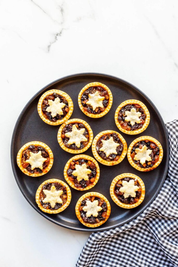 A black plate with mince pies and a black and white checkered linen.