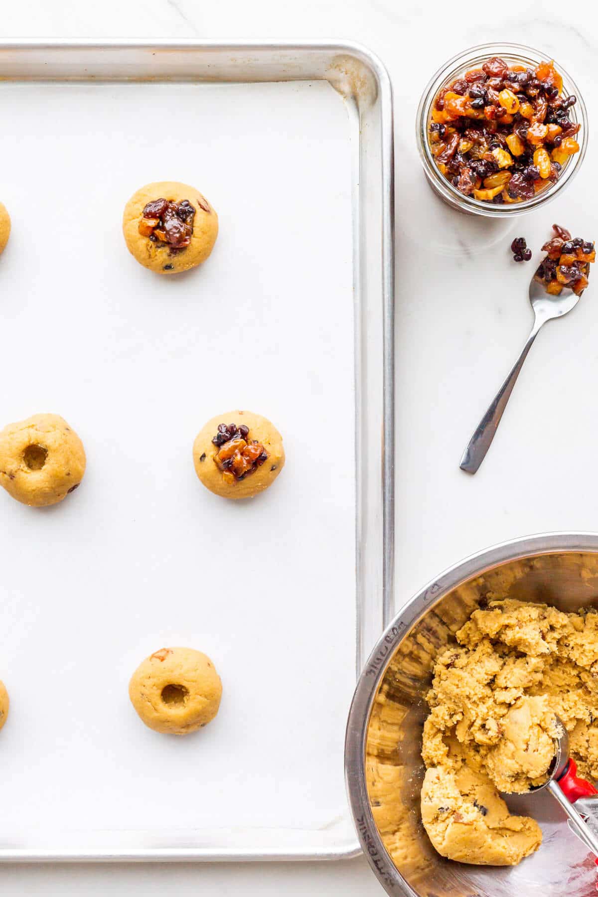 Scooping mincemeat cookie dough and topping with more mincemeat before baking.