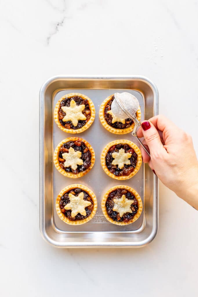 Sprinkling powdered sugar over freshly baked mince pies.