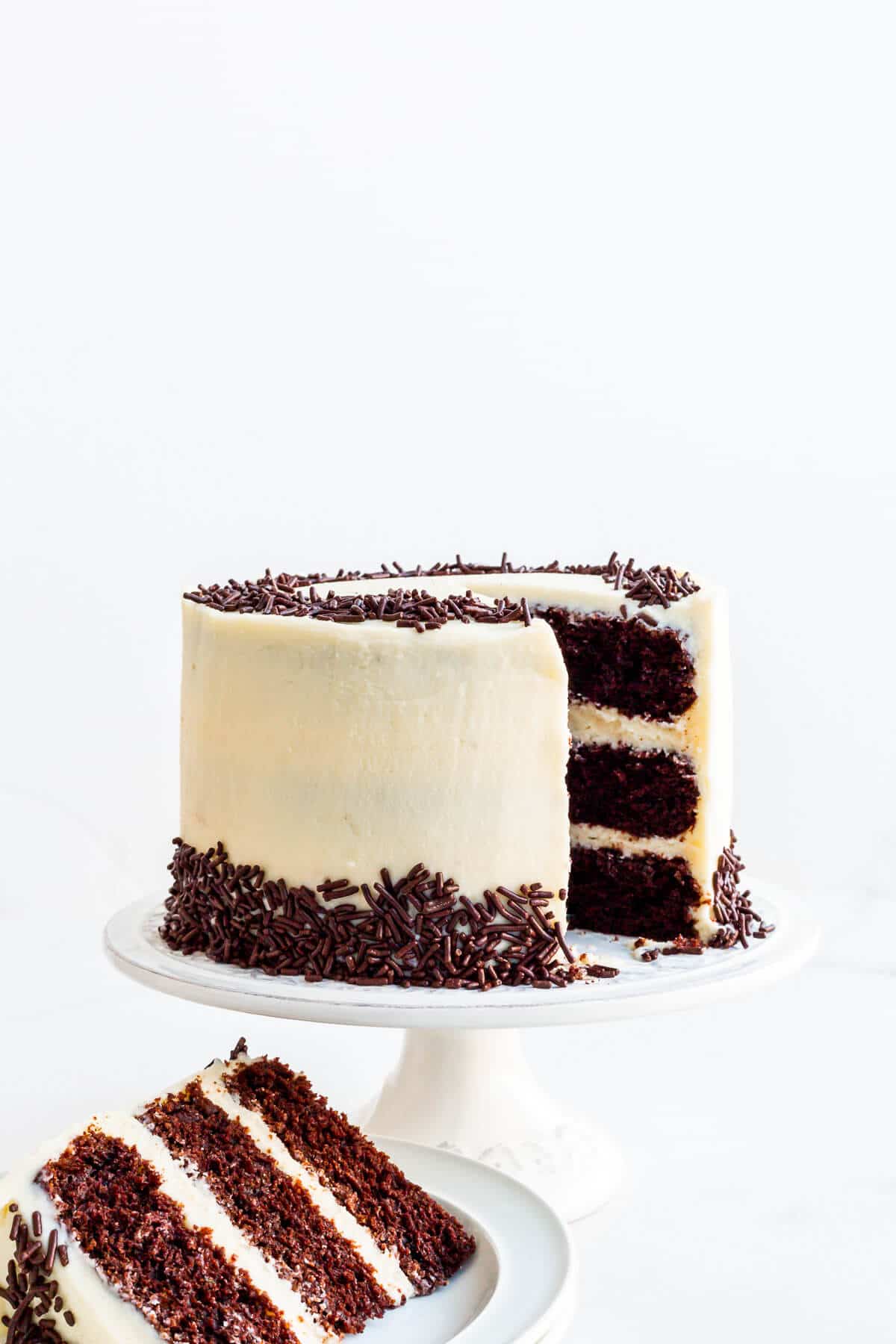 Chocolate layer cake with cream cheese frosting and chocolate sprinkles being served on plates.