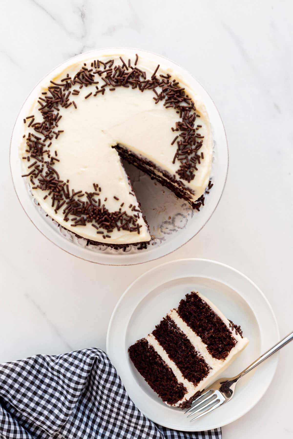 Chocolate layer cake with cream cheese frosting and chocolate sprinkles being served on plates.