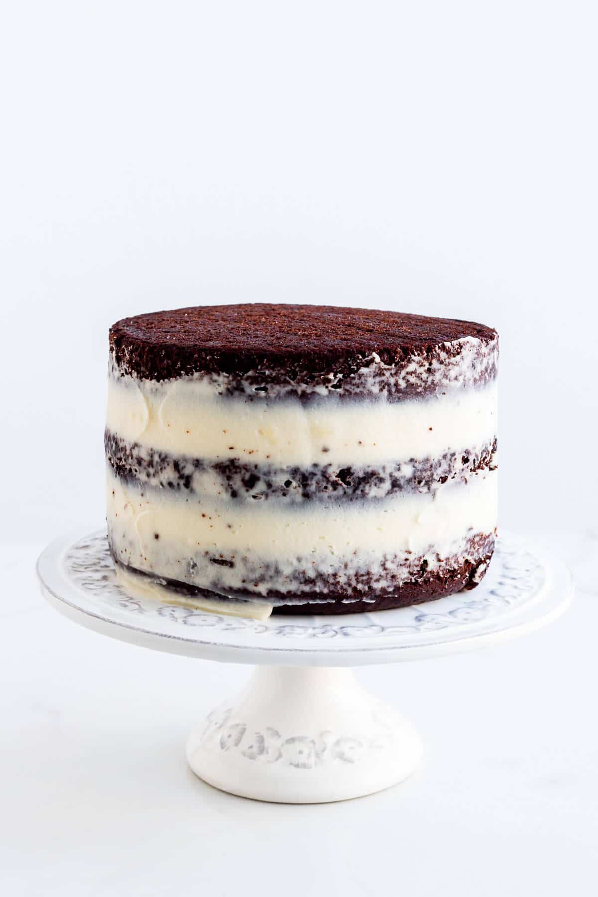 A naked chocolate layer cake with cream cheese frosting on a cake stand.