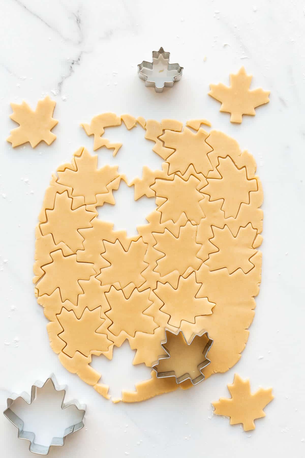 Cutting out maple leaf-shaped cookie dough with a cookie cutter to make maple leaf cookies.