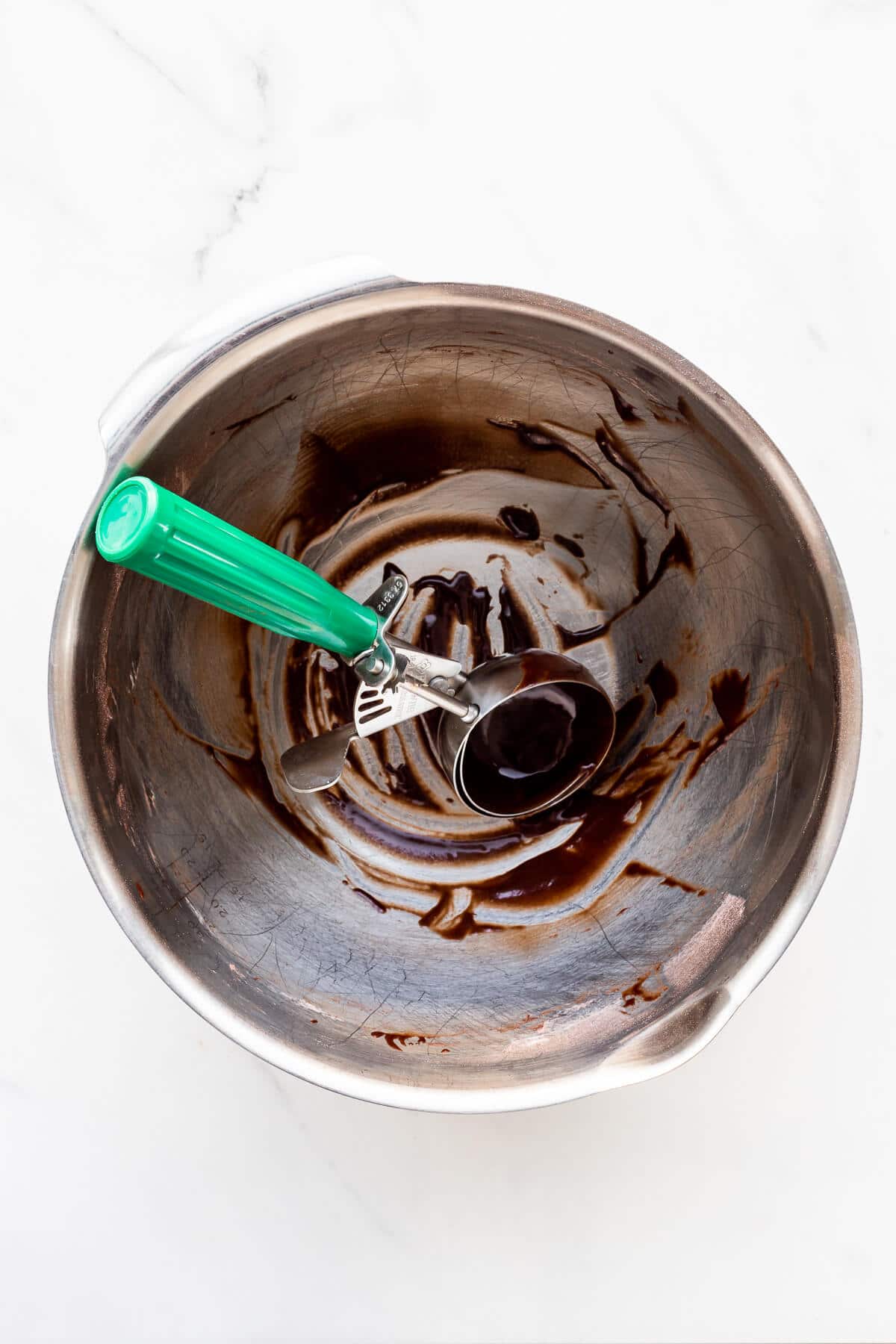 A bowl that had chocolate cake batter in it, scraped clean with a disher.