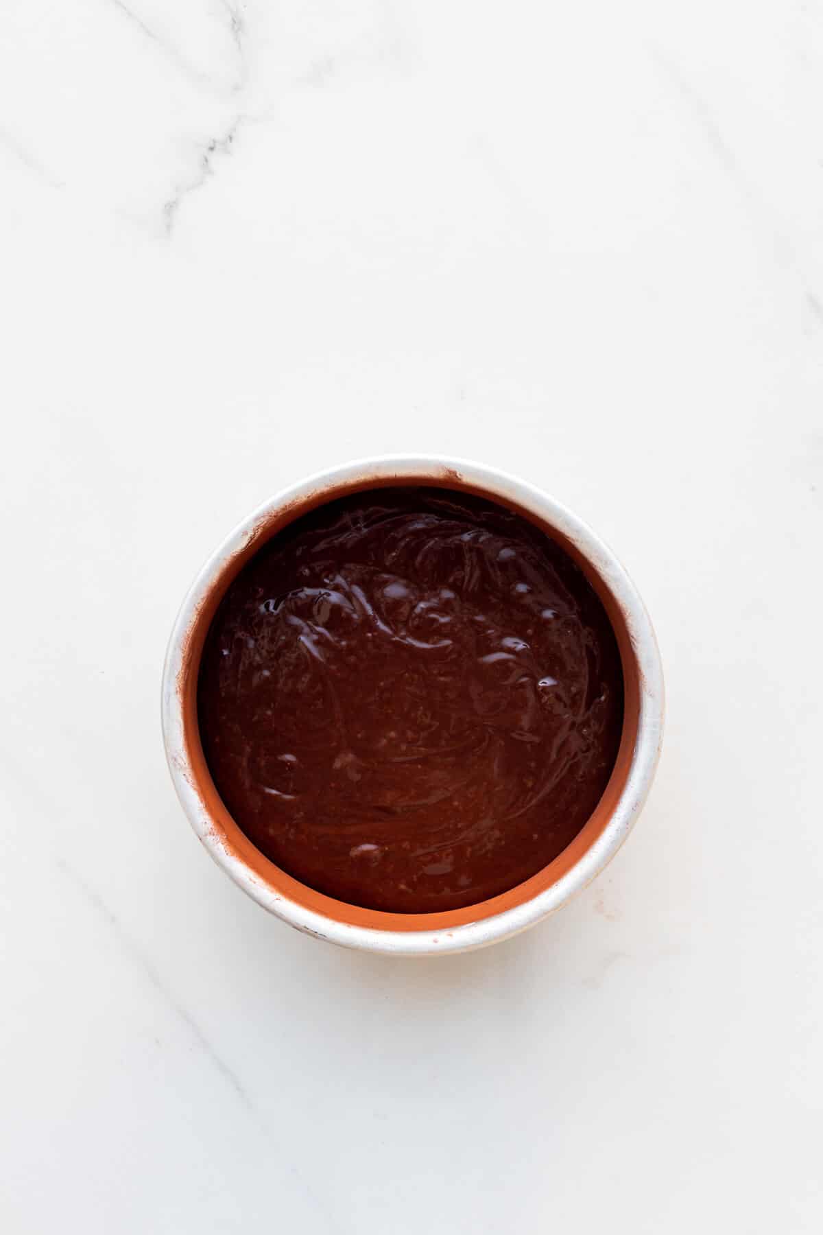 A cake pan with chocolate cake batter in it, ready to be baked.