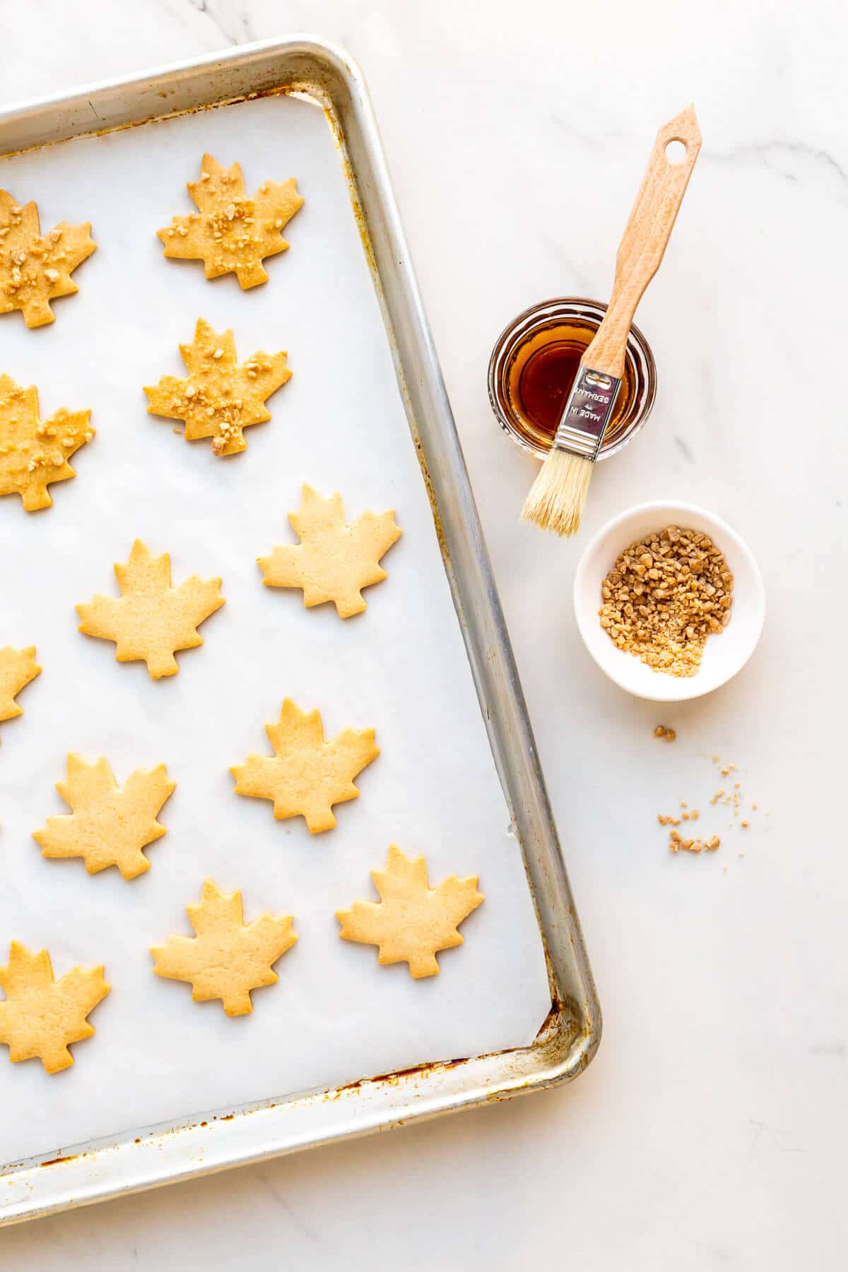 Glazing maple shortbread cookies with maple syrup and sprinkling with maple flakes to add more flavour before serving.