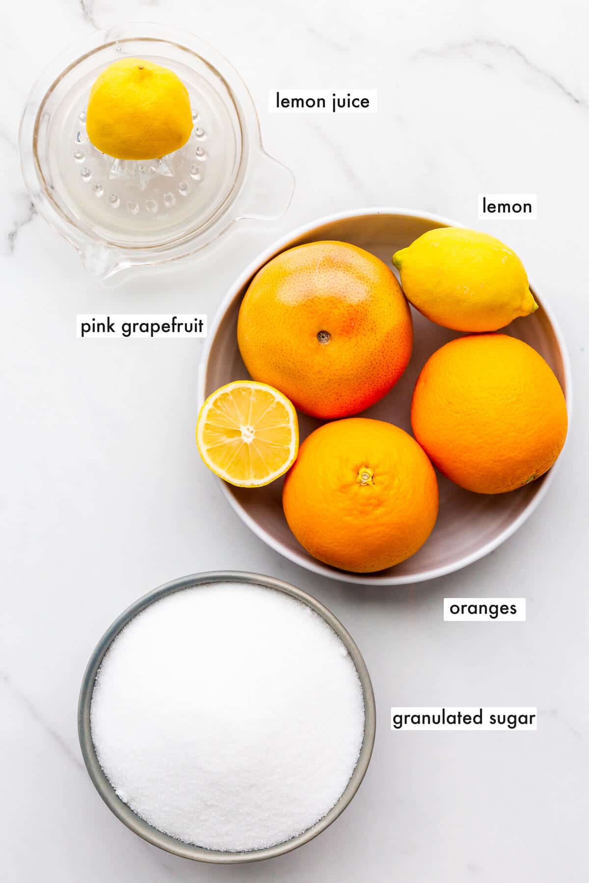 Ingredients to make three fruit marmalade from whole citrus fruit (two oranges, a grapefruit, and a lemon), sugar, and lemon juice.