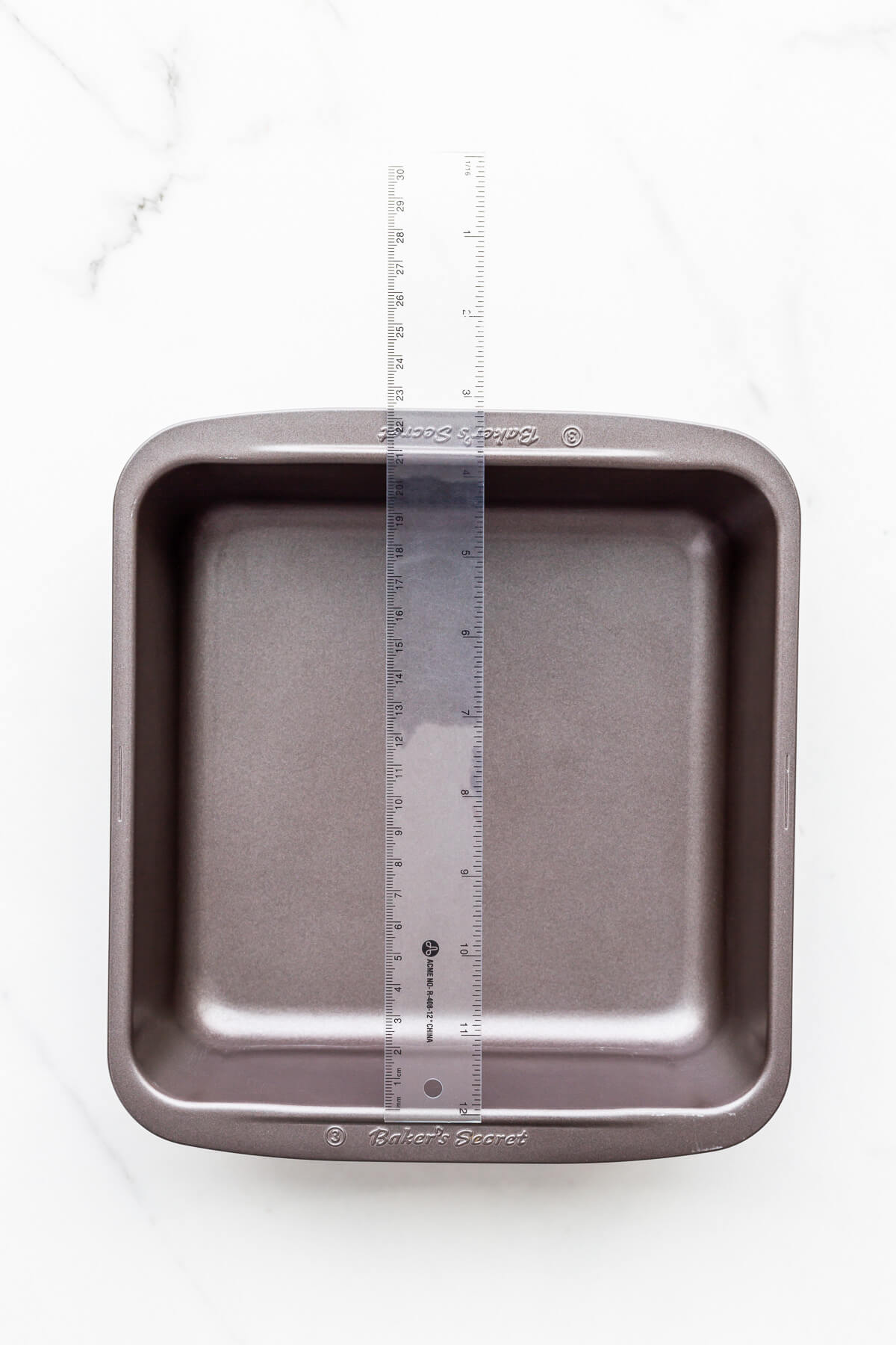 https://bakeschool.com/wp-content/uploads/2022/01/Measuring-the-size-of-a-square-cake-pan-with-a-ruler.jpg