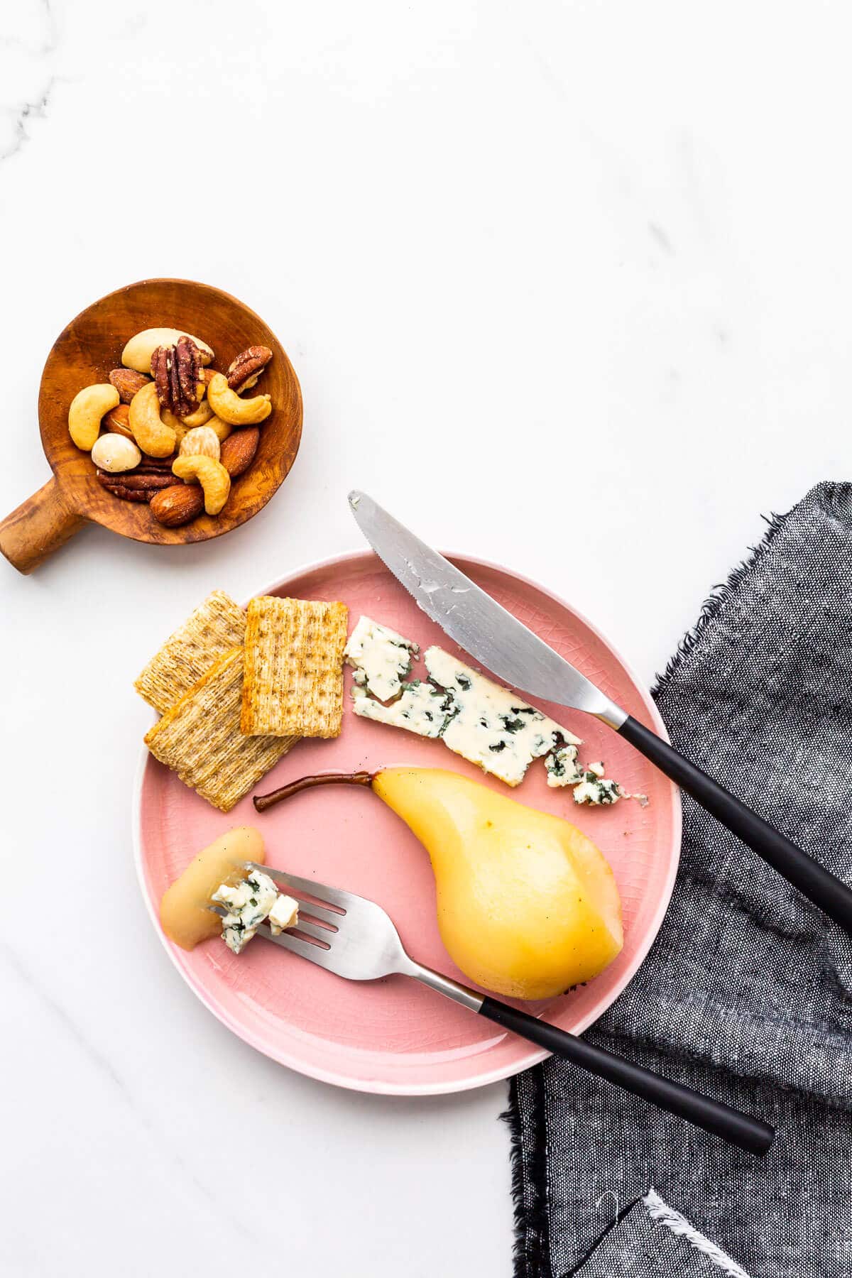 Poached pear on a pink plate with blue cheese, crackers, and toasted nuts.