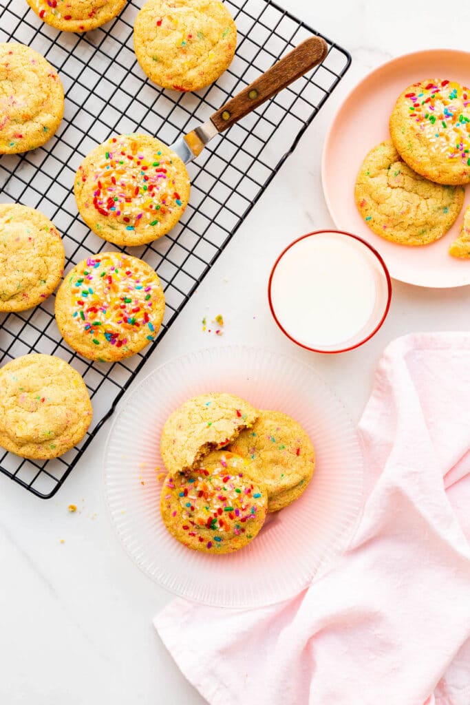 Sugar cookies with sprinkles, served on pink plates with a glass of milk.