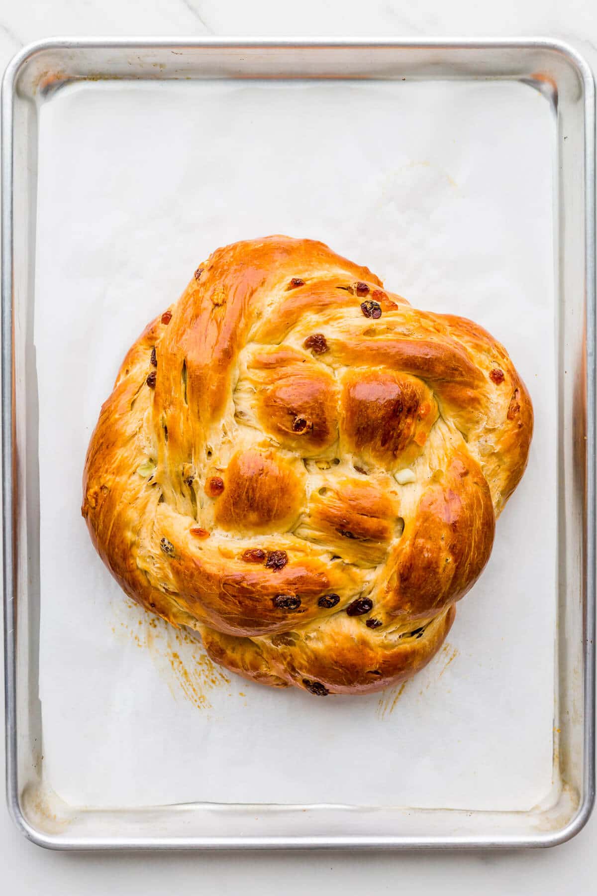 A braided boule of raisin bread, freshly baked on a sheet pan and golden brown.