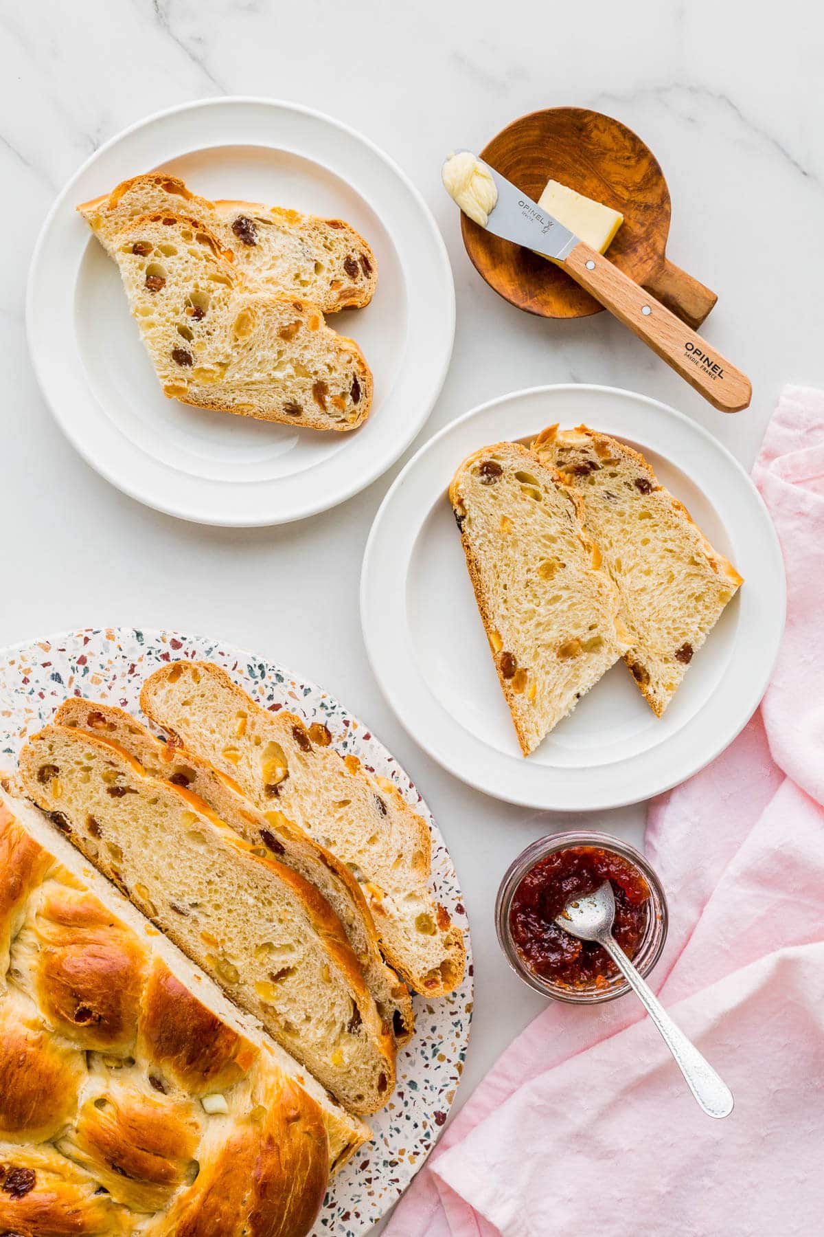 Slices of fruit bread served on white plates with butter and jam.