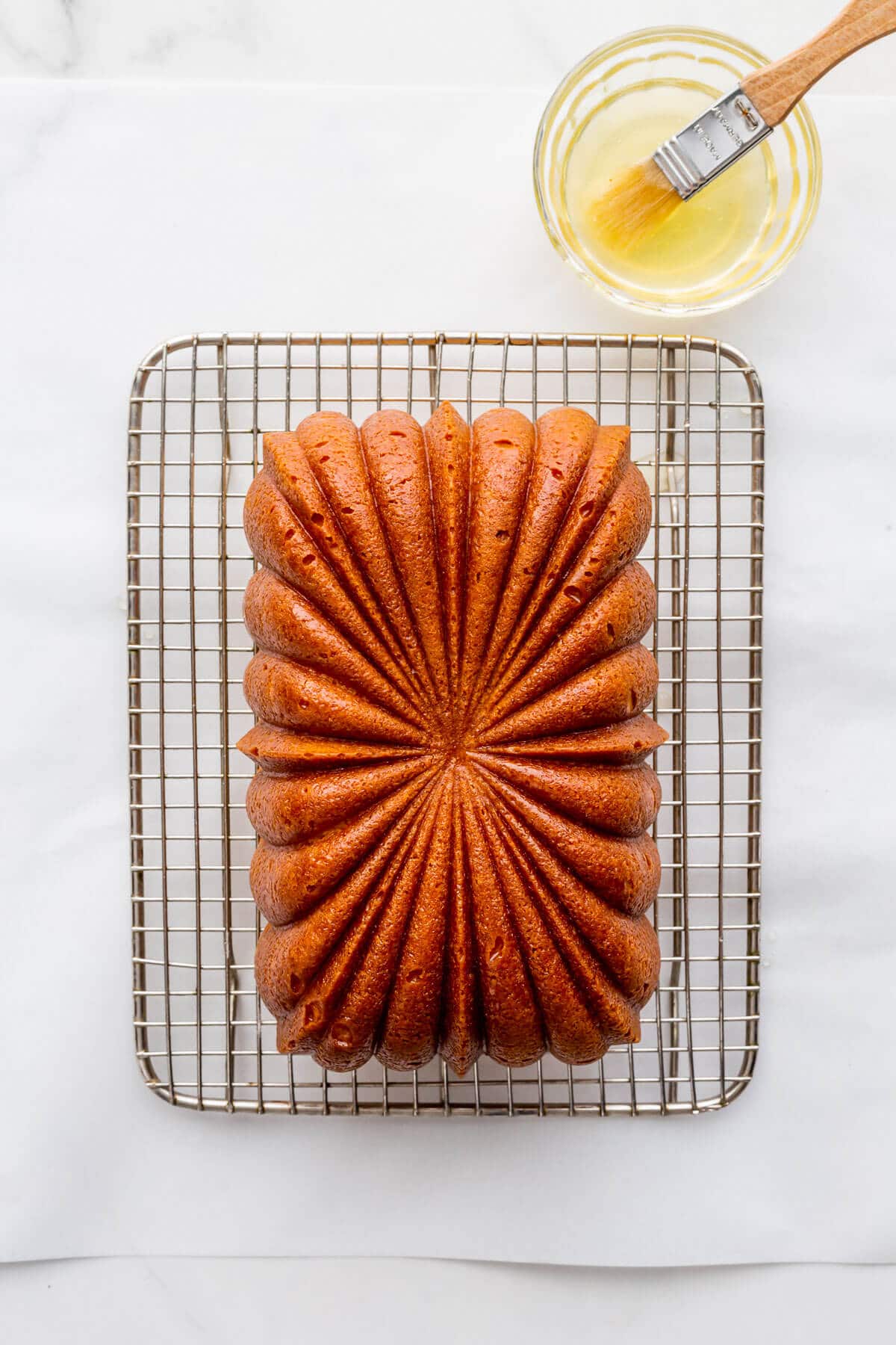 Lemon cake brushed with lemon syrup on a cooling rack.