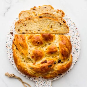 A round braided boule of Christmas fruit bread on a board, sliced.