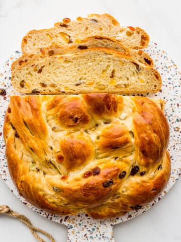 A round braided boule of Christmas fruit bread on a board, sliced.
