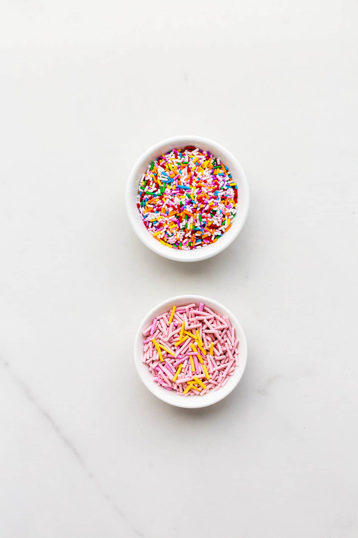 Rainbow jimmies (with vibrant colour) and homemade sprinkles (pastel colours) in small bowls.