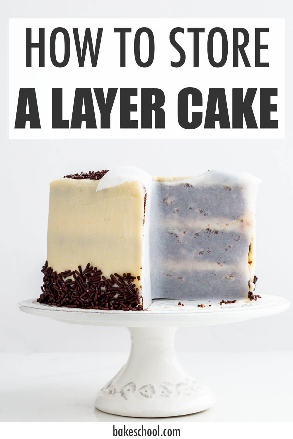 A layer cake on a cake stand, with parchment paper pressed up on the cut sides of the cake to help prevent drying.