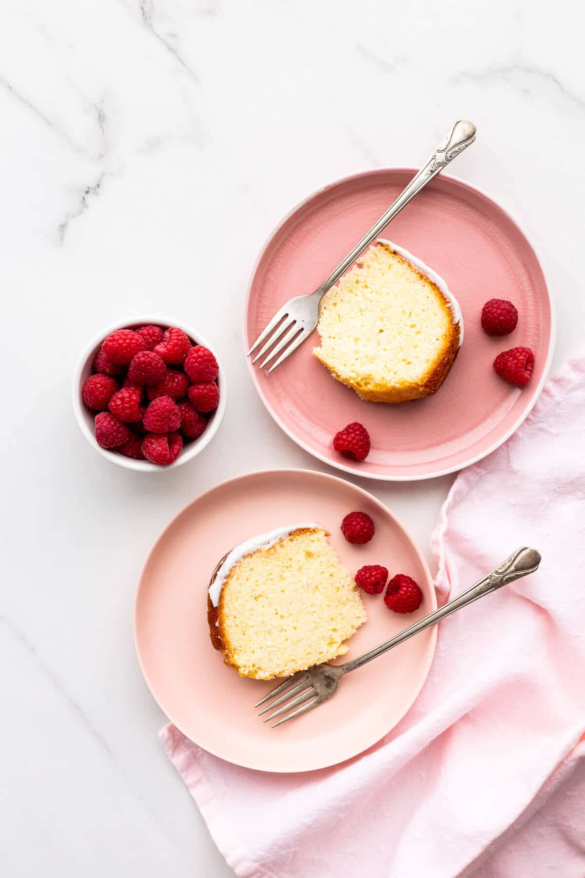 Slices of lemon cake on pink plates, served with raspberries.
