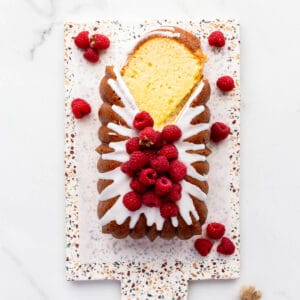 Lemon loaf cake topped with lemon icing and fresh raspberries being sliced to serve it