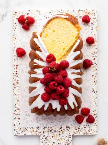 Lemon loaf cake topped with lemon icing and fresh raspberries being sliced to serve it