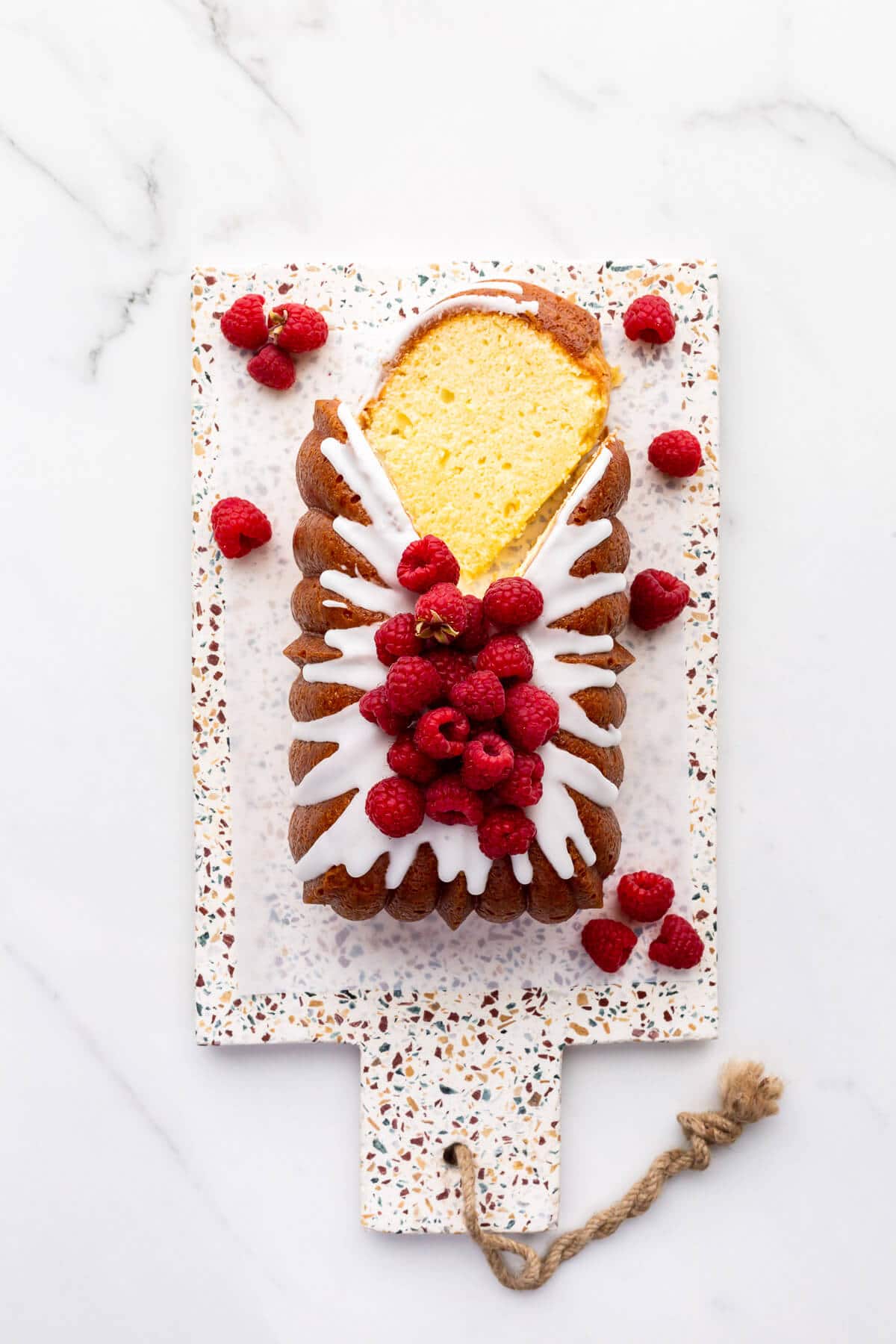 Iced lemon loaf cake on a terrazzo board being sliced.