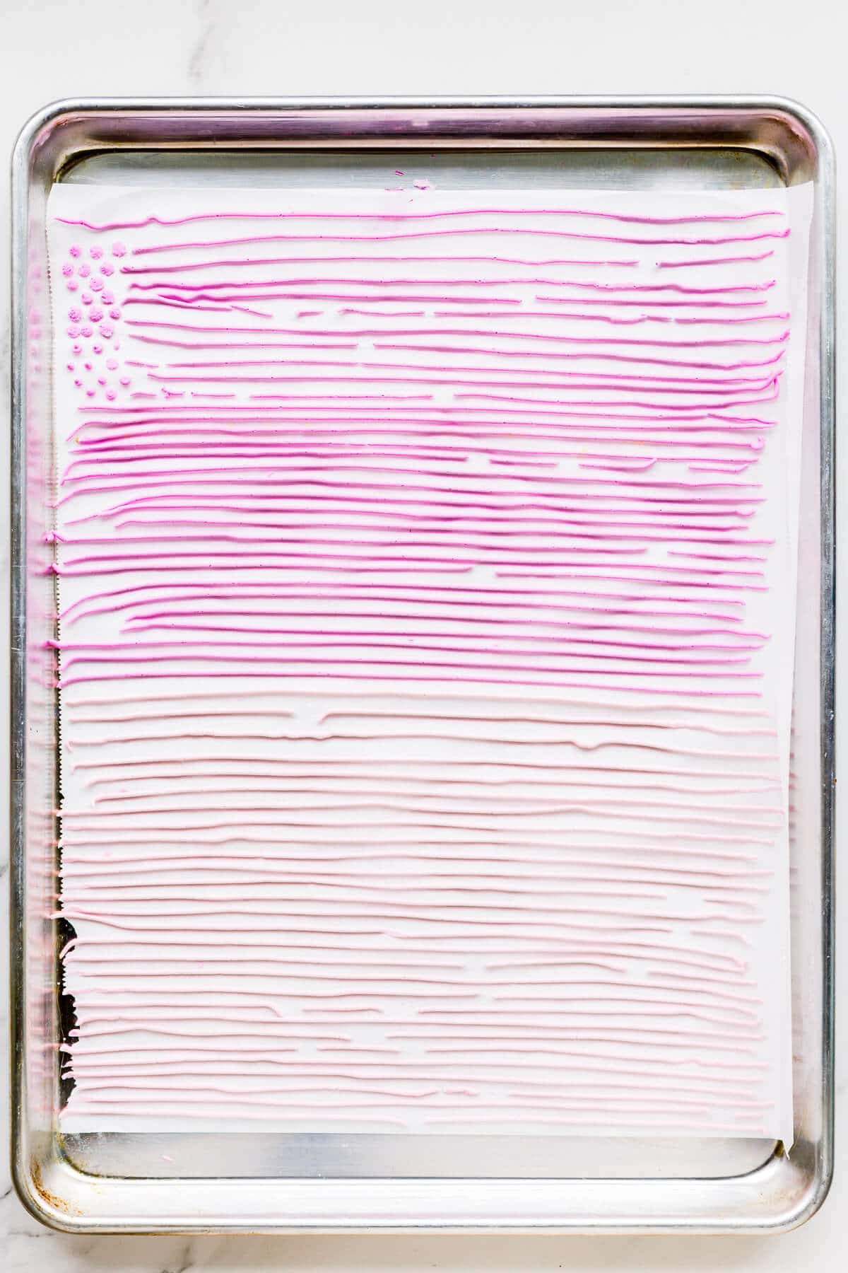 Pink royal icing piped in lines on parchment paper to make homemade sprinkles.