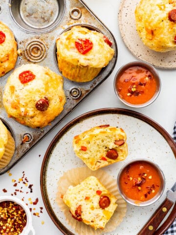 Serving pizza muffins on plates with marinara dipping sauce and chilli flakes.
