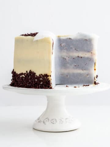 A layer cake on a cake stand, with parchment paper pressed up on the cut sides of the cake to help prevent drying.