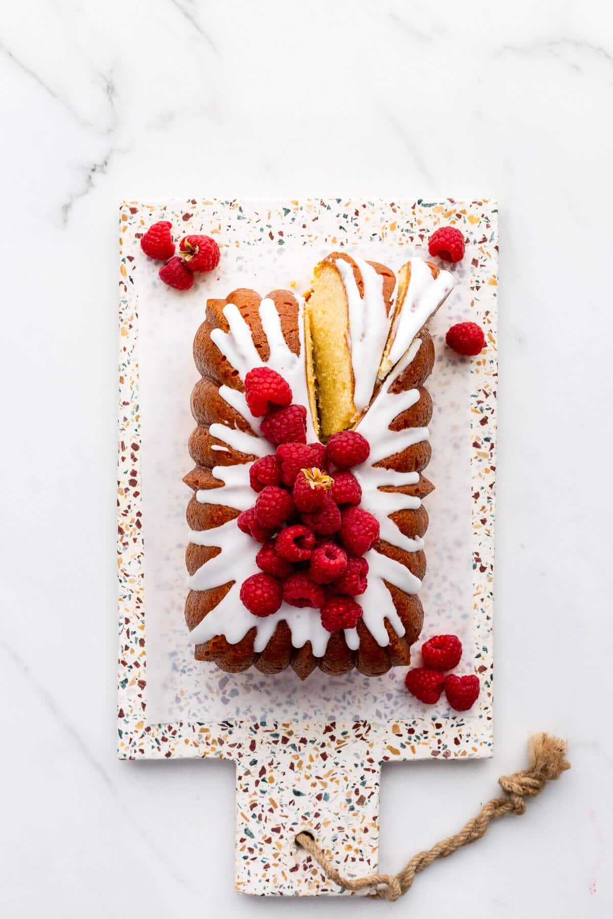 Lemon loaf cake topped with lemon icing and fresh raspberries being sliced to serve it