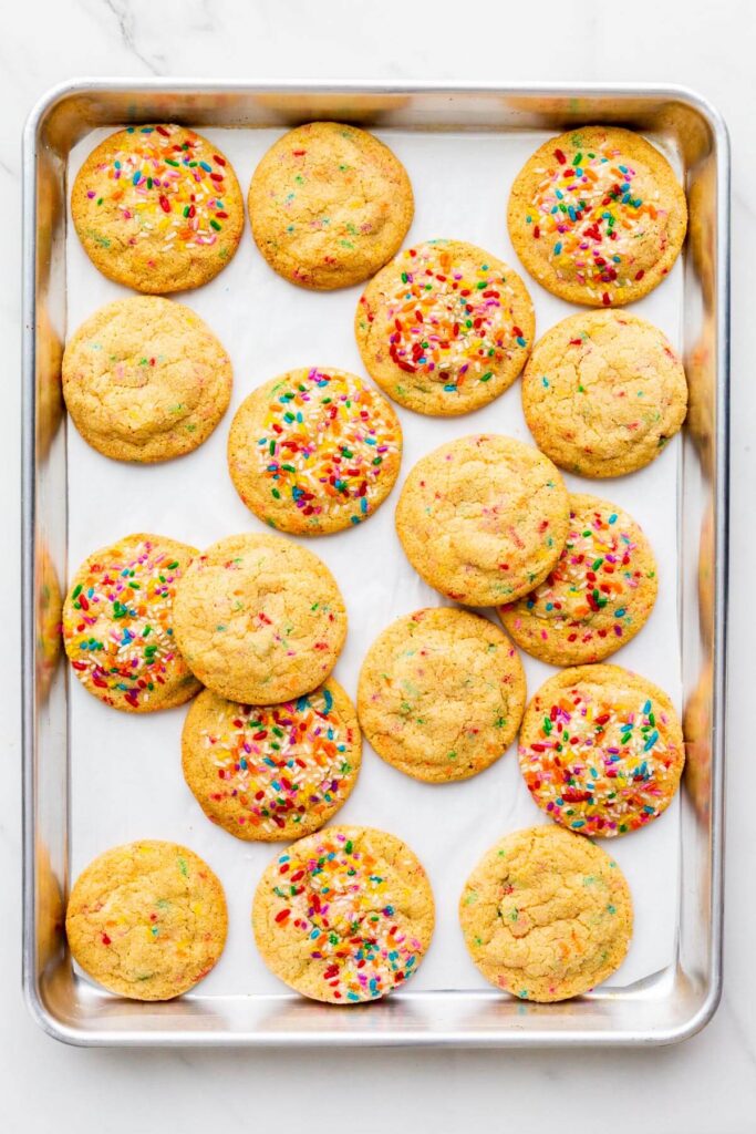 Freshly baked sugar cookies with sprinkles on a parchment-lined sheet pan.